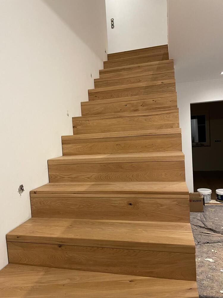 Eine Holztreppe an einer weißen Wand führt nach oben in das Obergeschoss eines Gebäudes.