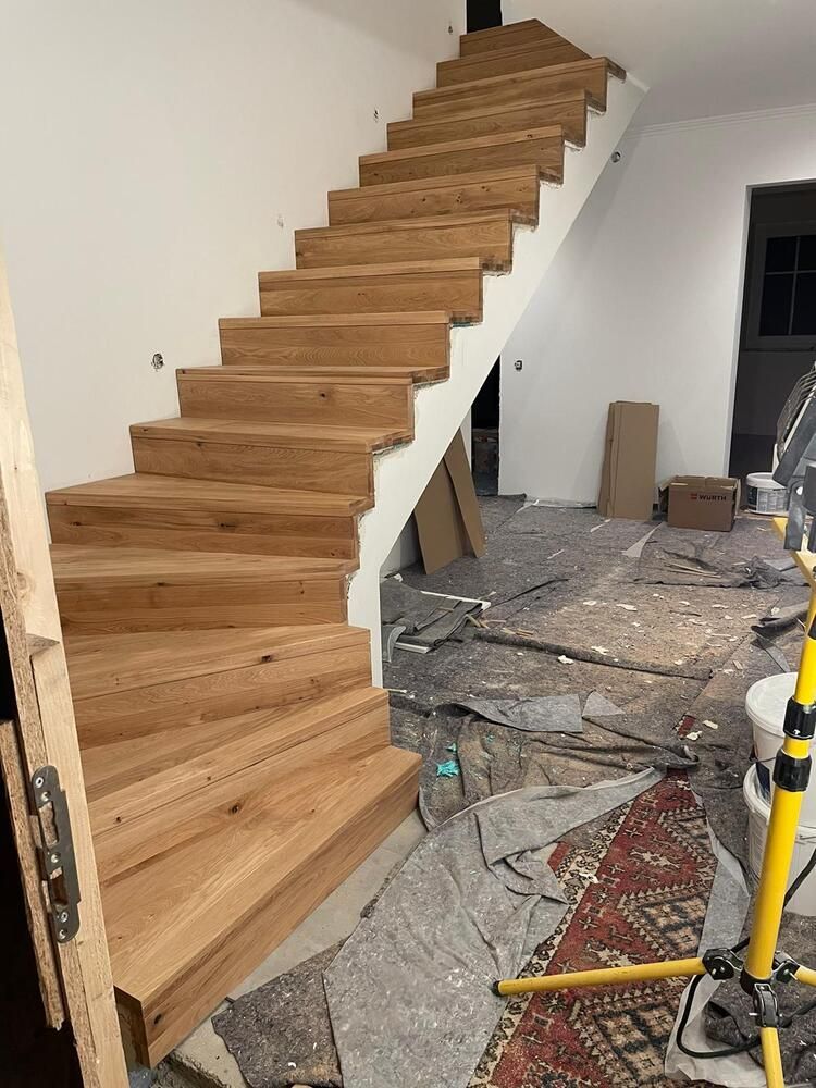 Im Bau befindliche Holztreppe; weiße Wände; Bauschutt auf dem Boden.