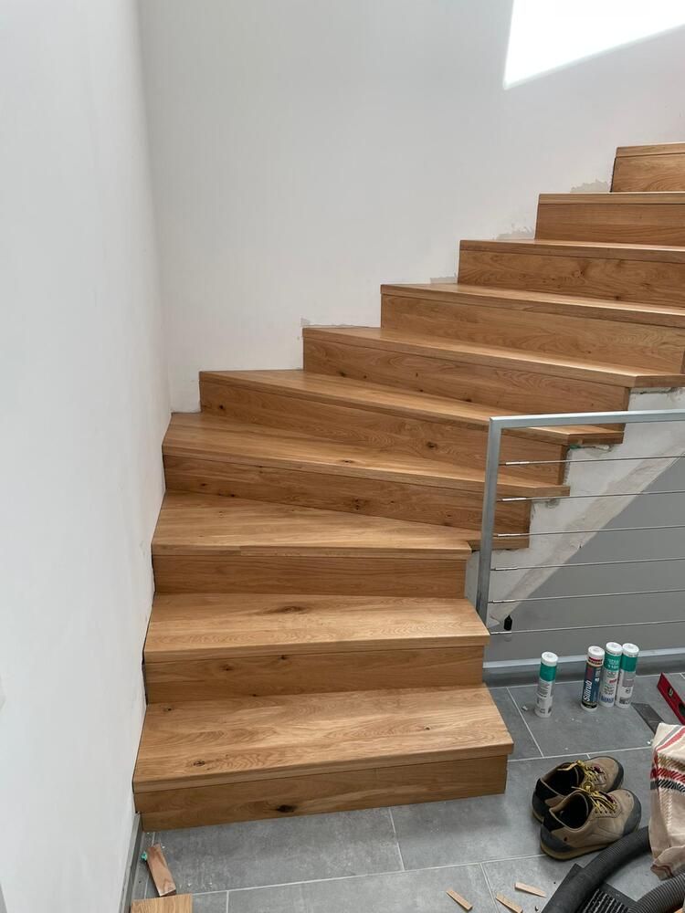 Holztreppe in modernem Design vor einer weißen Wand und einem teilweisen Metallgeländer.