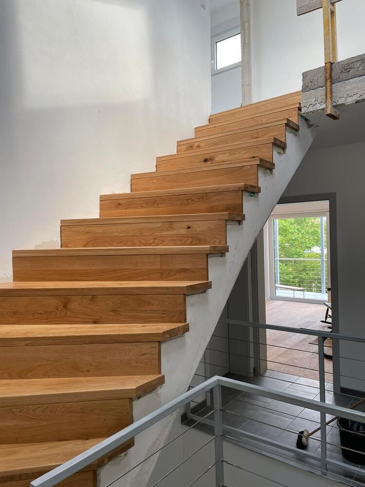 Holztreppe mit weißen Wänden, die nach oben führt. Silbernes Geländer am unteren Ende.