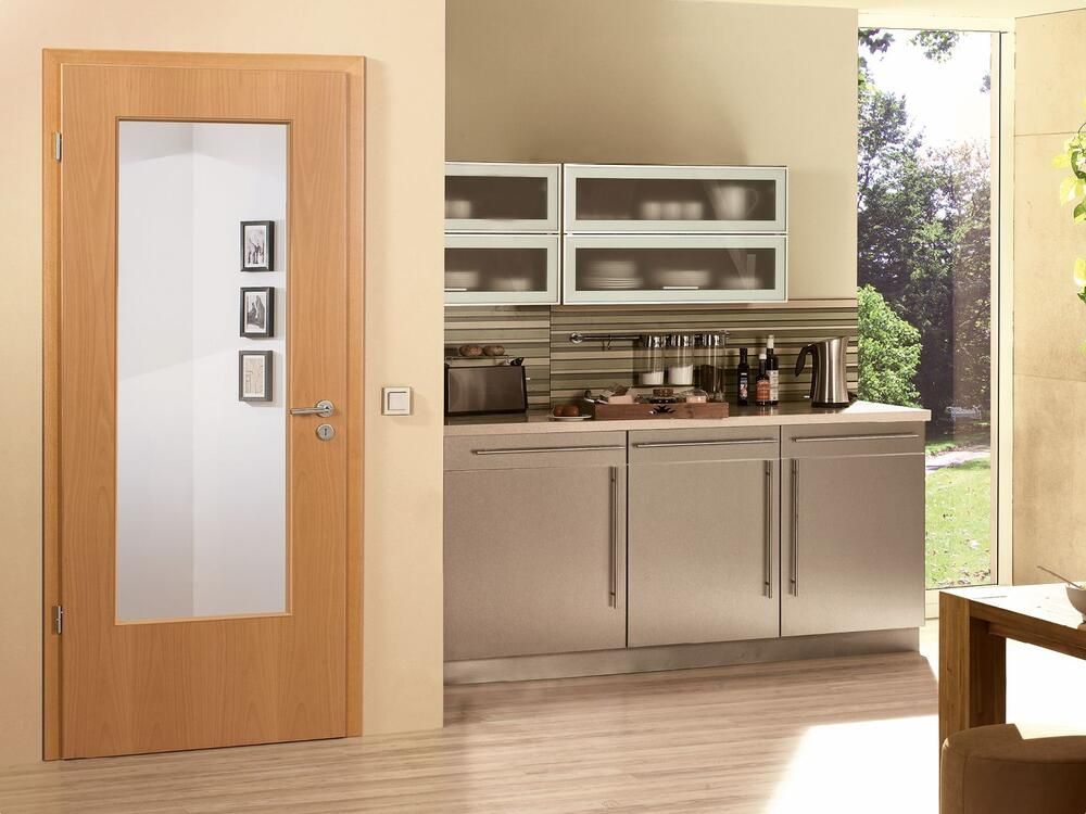 Eine Holztür mit Milchglasscheibe führt in eine Küche mit Edelstahlschränken und einem Fenster.