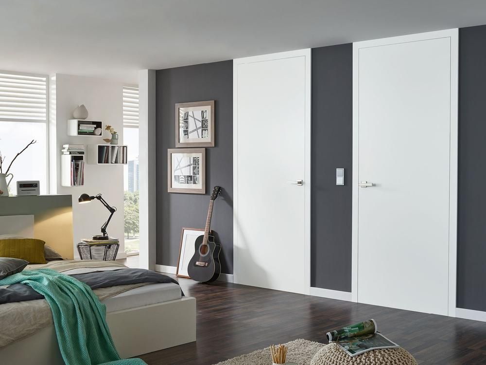 Modernes Schlafzimmer mit weißen Türen, dunkelgrauer Akzentwand, Gitarre und Bett mit türkisfarbener Decke.