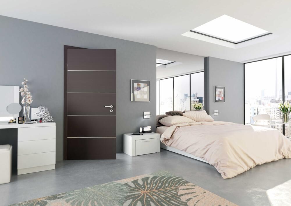 Modernes Schlafzimmer mit grauen Wänden, brauner Tür, Bett mit beiger Bettwäsche und einem Dachfenster.