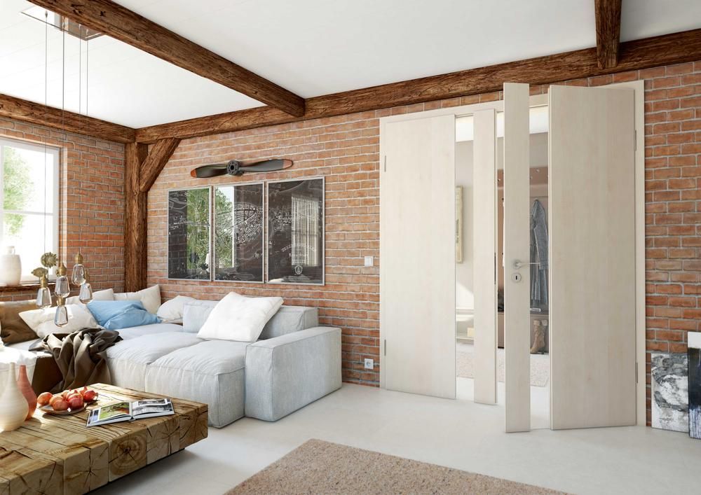 Wohnzimmer mit freigelegten Ziegelwänden, hellfarbenem Sofa, Holzbalken und teilweise geöffneten, hellen Holztüren.