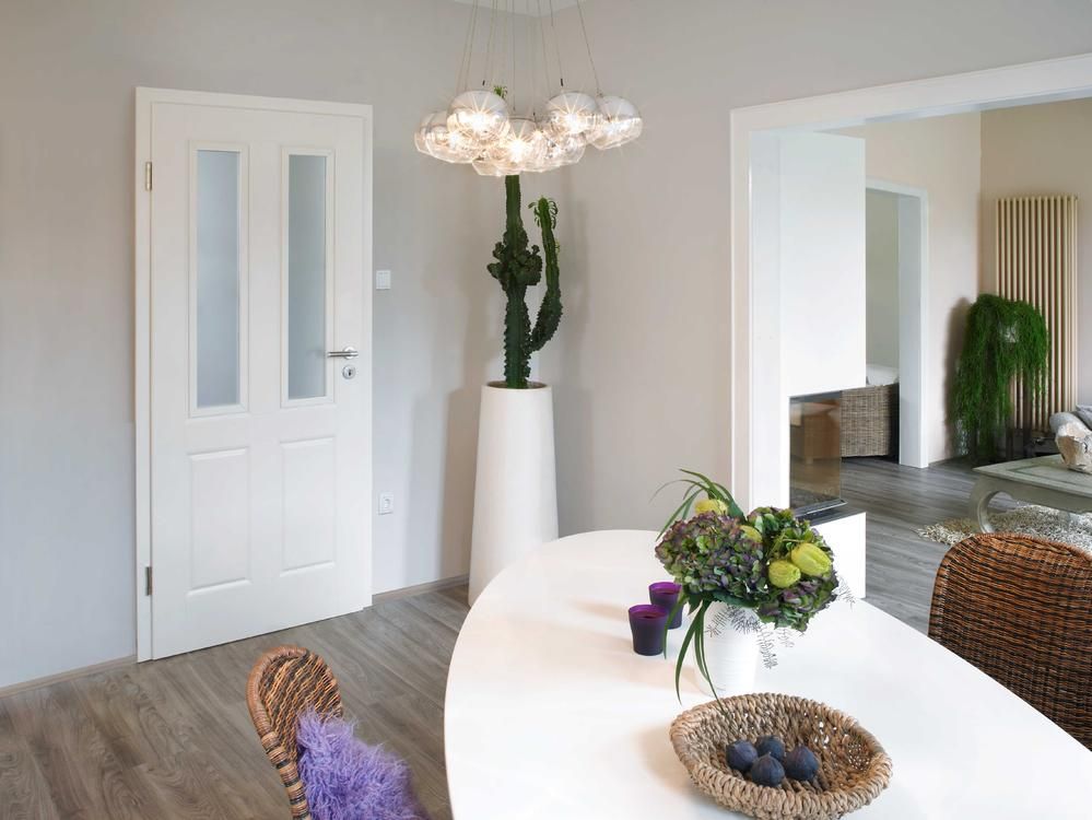 Weißes Esszimmer mit Tisch, Stühlen und einem hohen Kaktus.