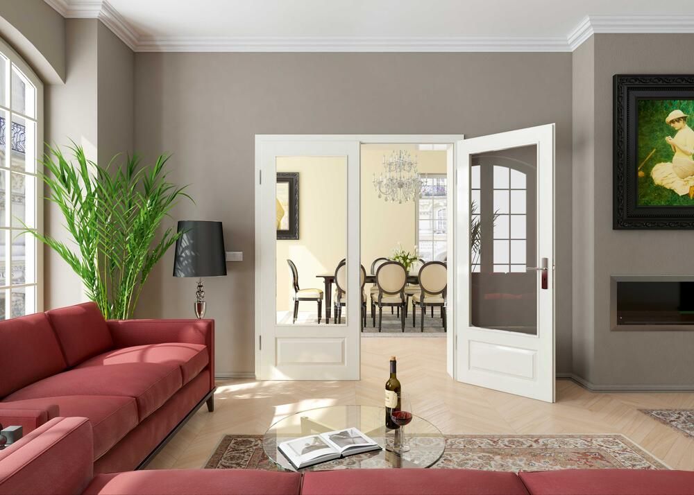 Wohnzimmer mit rotem Sofa, offene weiße Türen zum Essbereich. Grüne Pflanze, Tisch mit Wein, Gemälde.