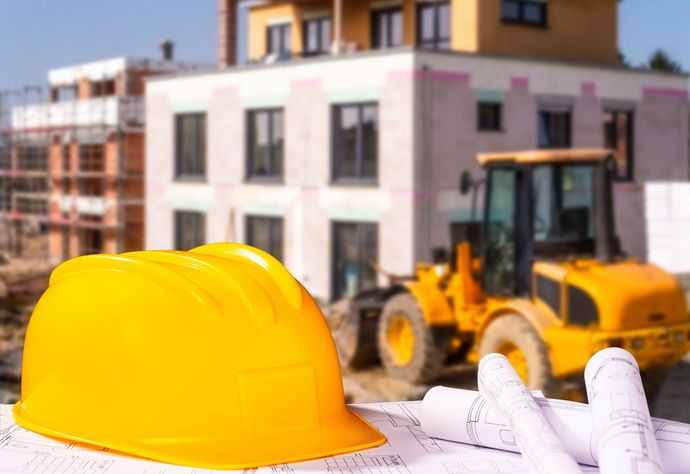 Auf einer Baustelle liegt ein gelber Bauhelm auf einem Stapel Baupläne.