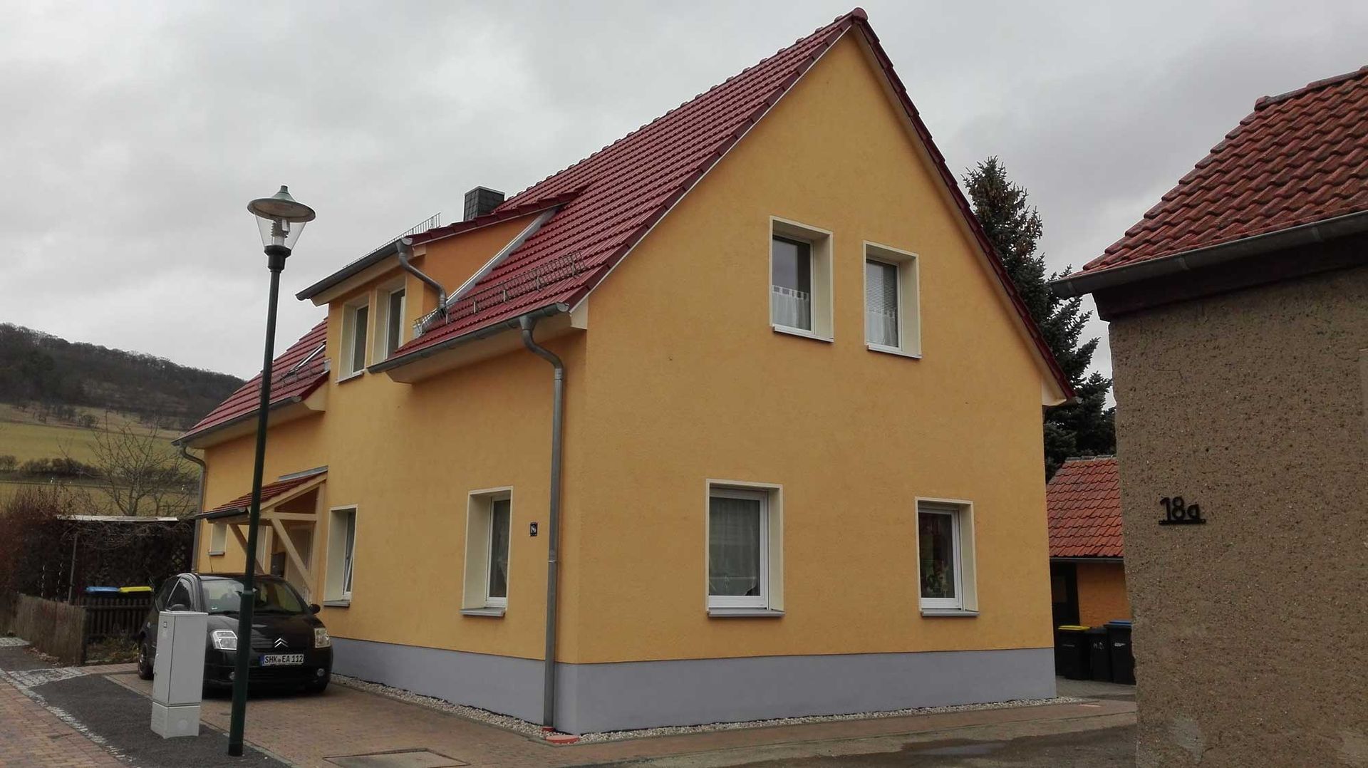 Ein gelbes Haus mit rotem Dach und einem davor geparkten Auto