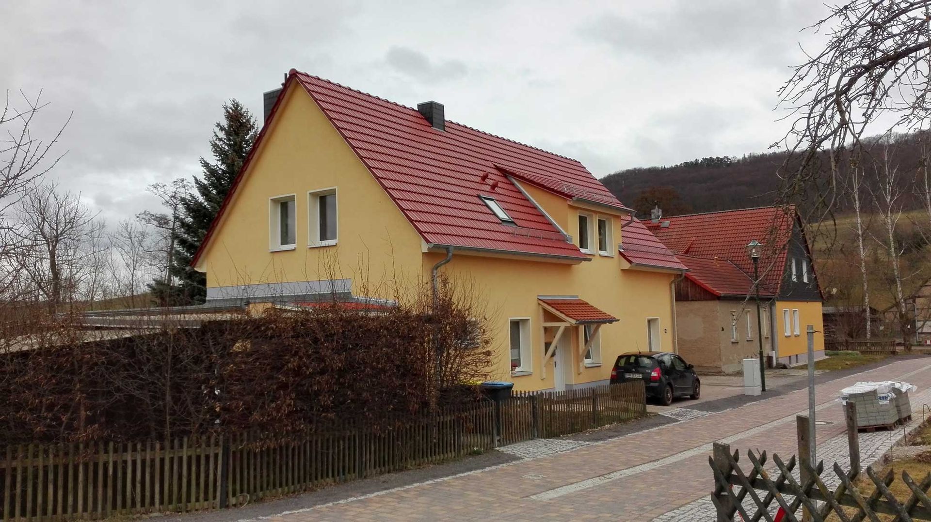 Ein gelbes Haus mit einem roten Dach und einem davor geparkten Auto.