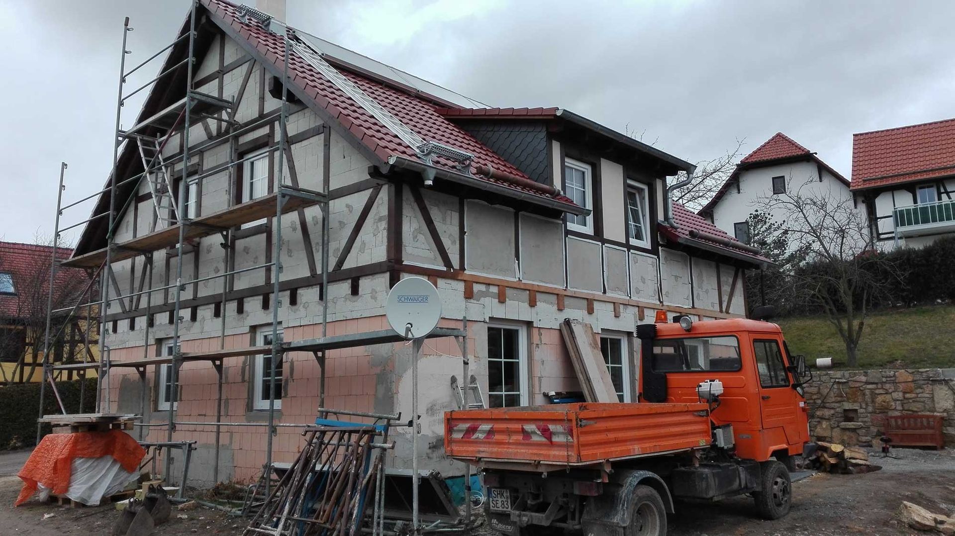 Ein orangefarbener Lastwagen steht vor einem im Bau befindlichen Gebäude.