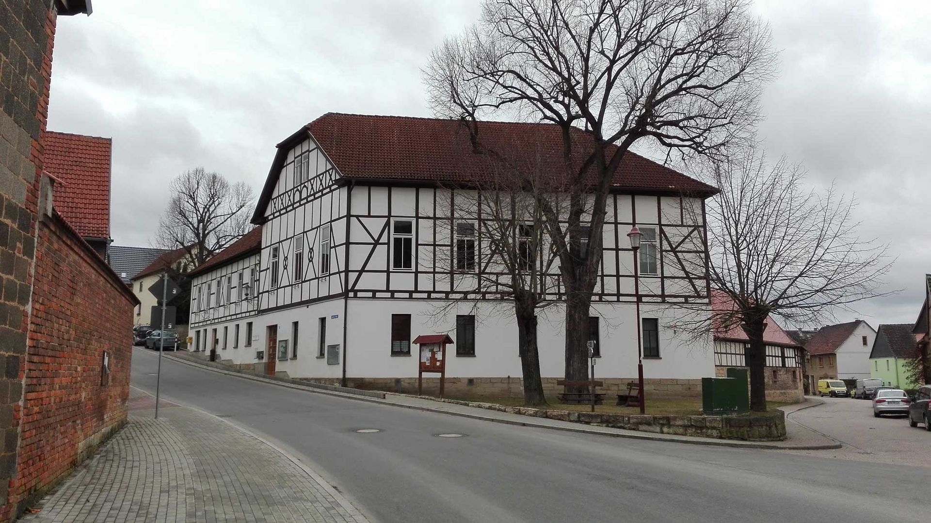 Am Straßenrand steht ein großes weißes Gebäude mit einem roten Ziegeldach.
