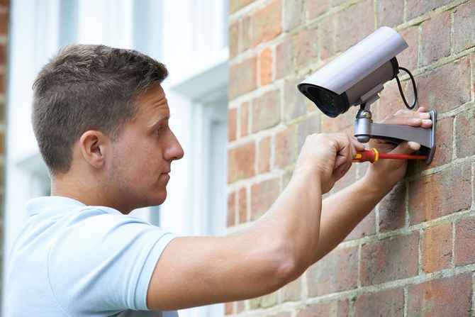 Mitarbeiter installiert eine Kamera an einer Wand Mitarbeiter installiert eine Kamera an einer Wand