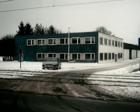 Zweistöckiges Geschäftsgebäude mit türkisfarbener und weißer Fassade in verschneiter Umgebung; davor ist ein Auto geparkt.