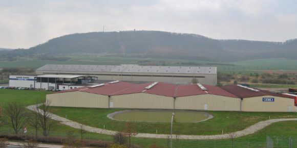 Gebäude mit roten Dächern auf einer grünen Wiese vor einem Hügel im Hintergrund an einem bewölkten Tag.