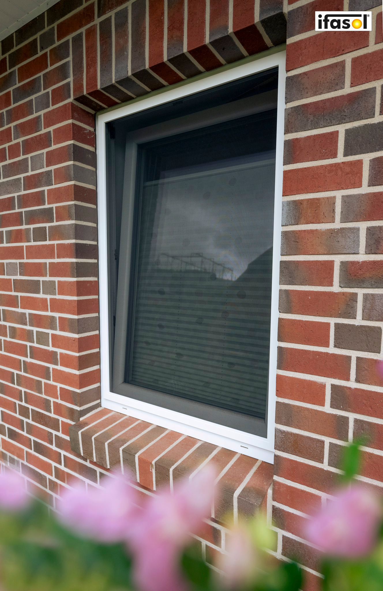 Eine Backsteinmauer mit einem Fenster und Blumen im Vordergrund.