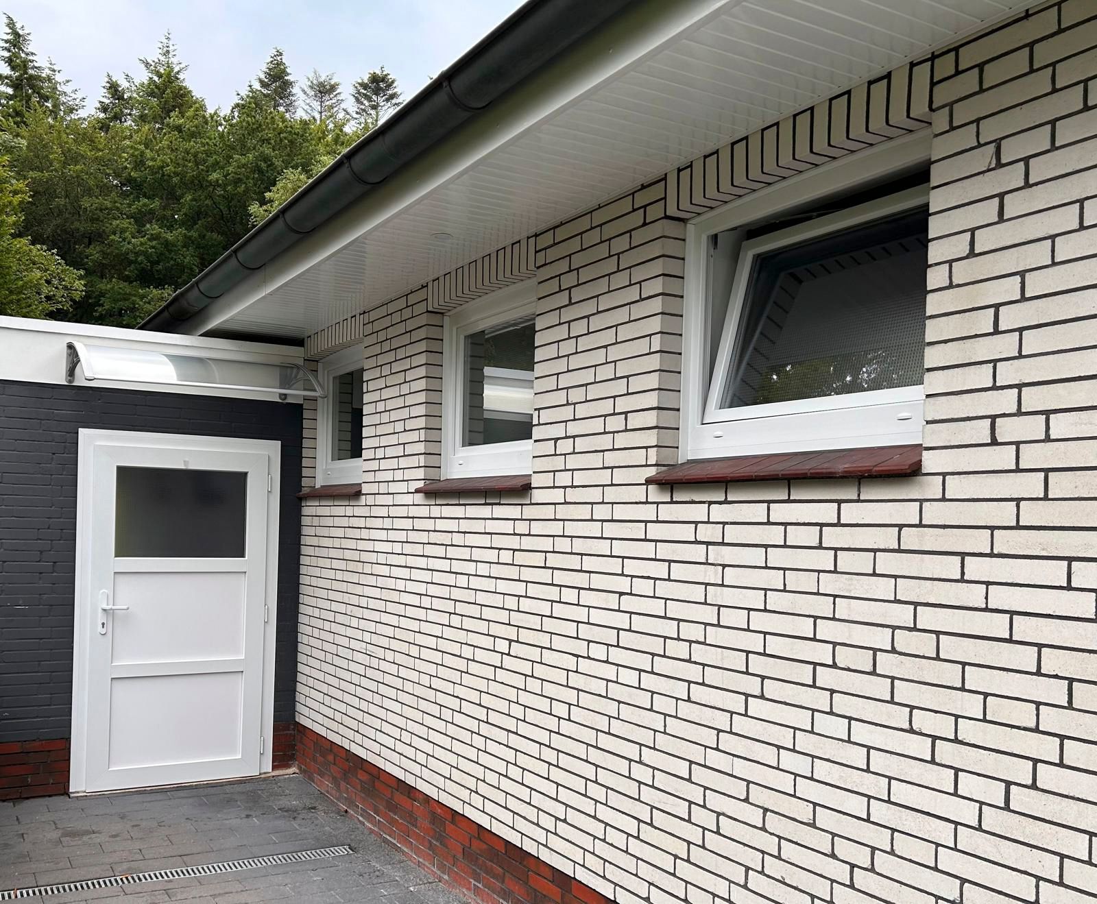 Ein weißes Backsteingebäude mit einer weißen Tür und Fenstern