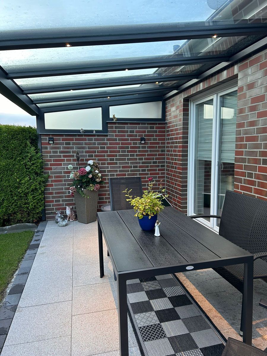 Eine Terrasse mit Tisch und Stühlen unter einem Glasdach.