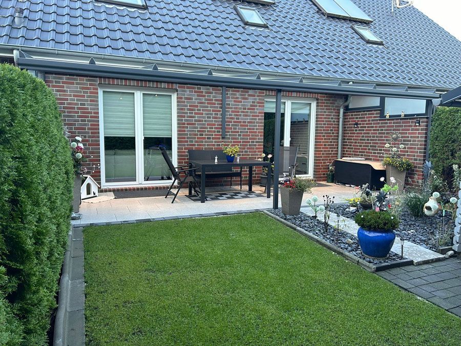 Eine Terrasse mit Tisch und Stühlen vor einem Backsteinhaus.