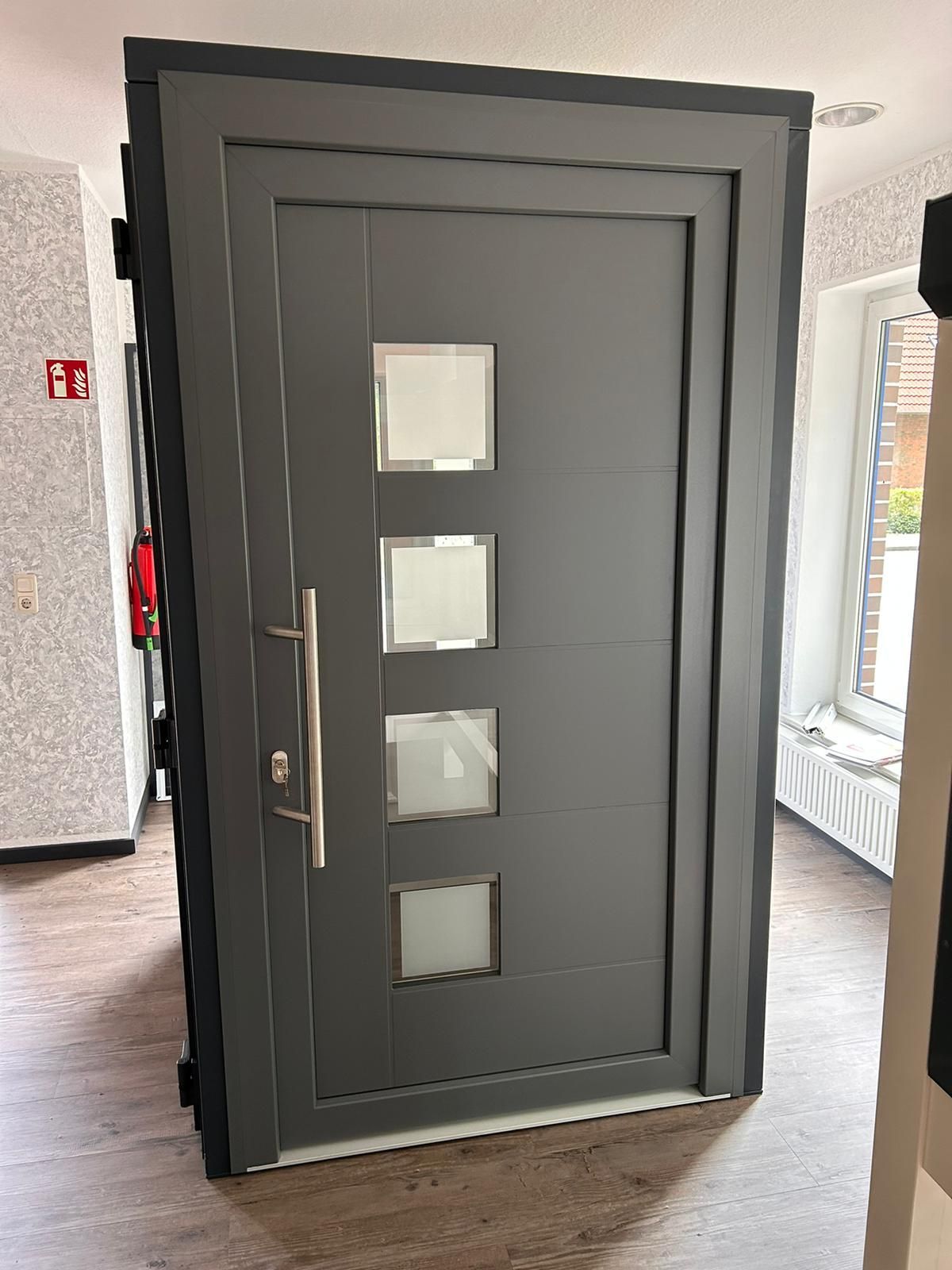 In einem Raum steht auf einem Holzboden eine graue Tür mit quadratischen Fenstern.