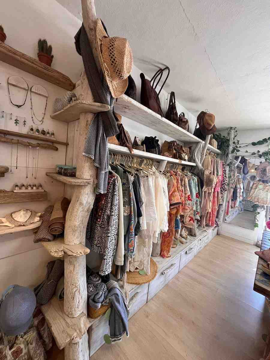 Interior de boutique con estantes de madera con sombreros, bufandas y bolsos tejidos a lo largo de un pasillo luminoso.