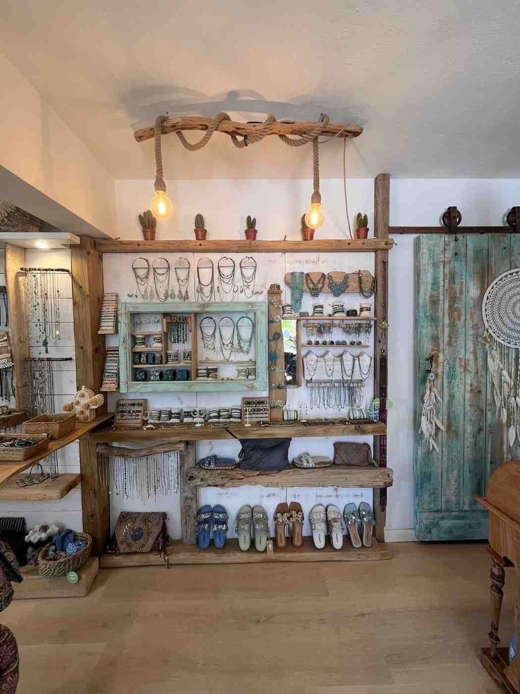 Exhibición rústica de tienda con luces colgantes, estantes con baratijas y una puerta turquesa en un interior acogedor.