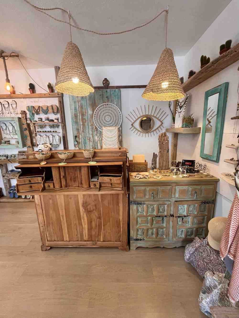 Interior de tienda bohemia con lámparas colgantes tejidas, armarios de madera y decoración colorida.