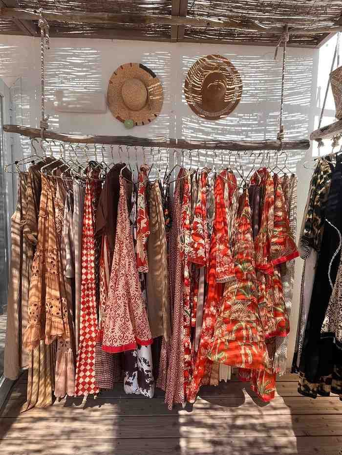 Un perchero con coloridos vestidos florales y sombreros expuestos en el escaparate de una boutique.