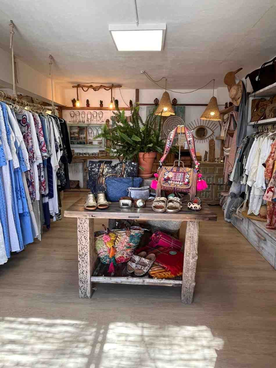 Interior de una boutique de ropa con percheros de vestidos, una mesa de exposición central y bolsos en los estantes.