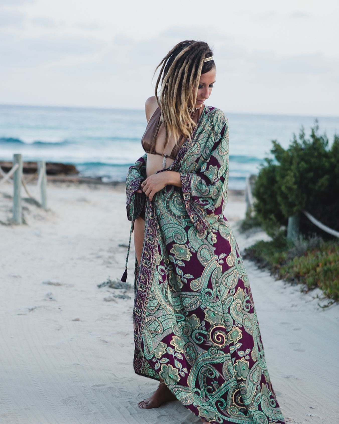 Una persona con un vestido estampado está de pie en la playa, mirando por encima del hombro con el océano de fondo.