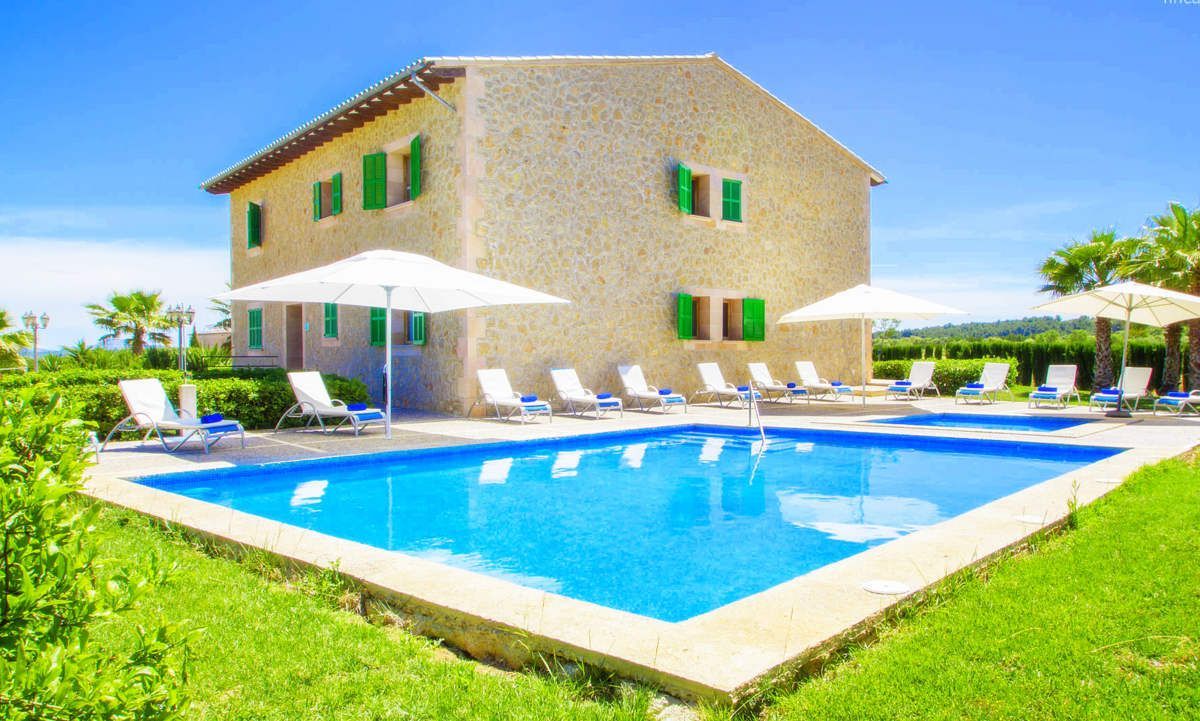 Luxury villa with green shutters beside a bright blue pool and sun loungers on a sunny day
