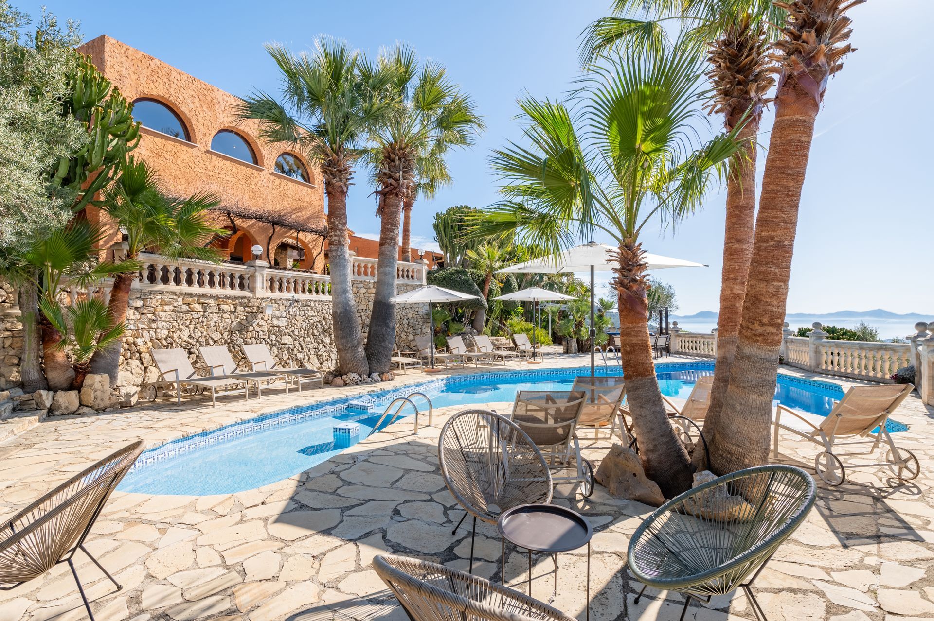 Tropical resort pool with palm trees, stone patio, lounge chairs, and ocean view