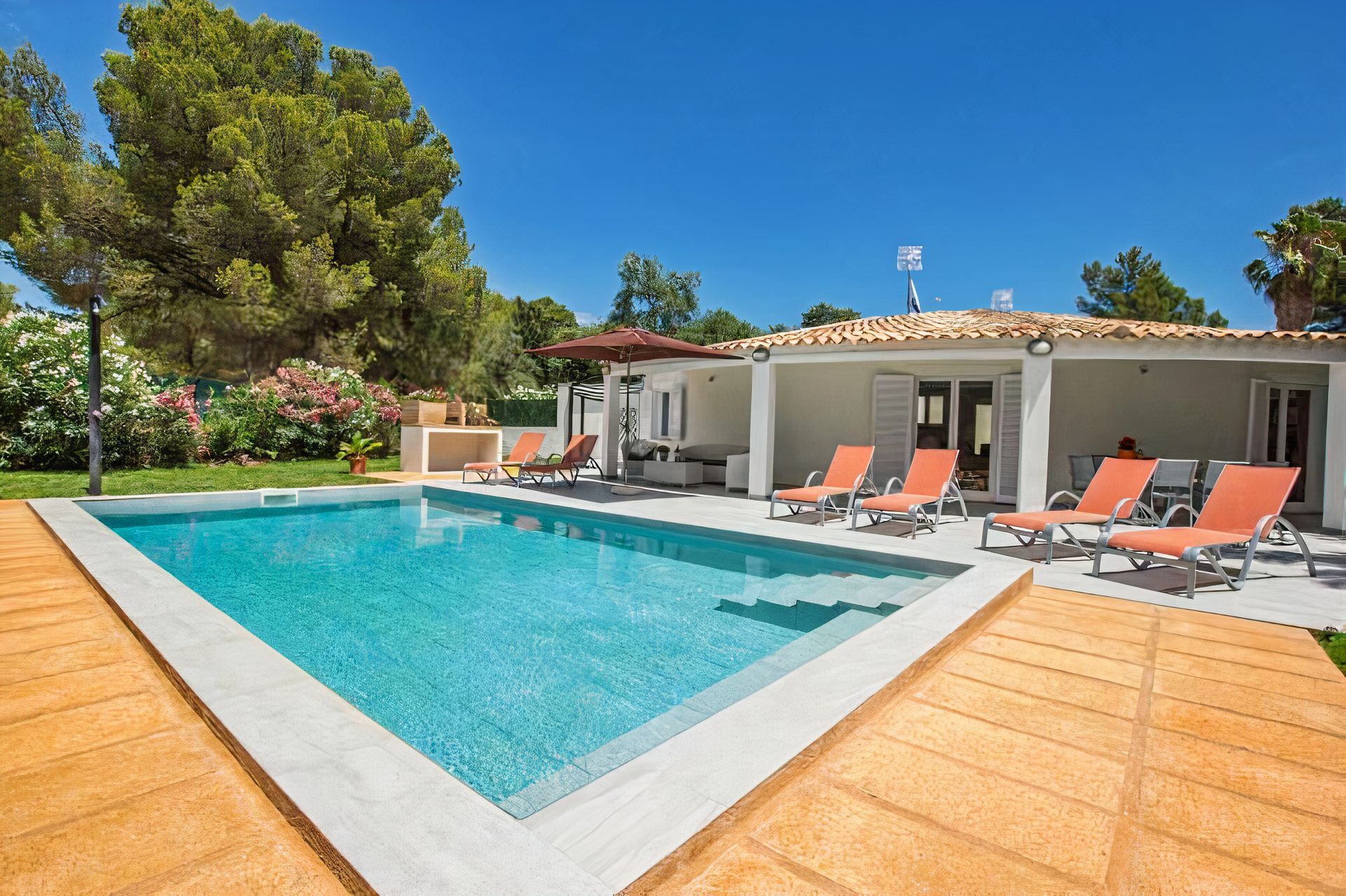 Modern villa patio with turquoise pool, orange loungers, and sunny garden setting
