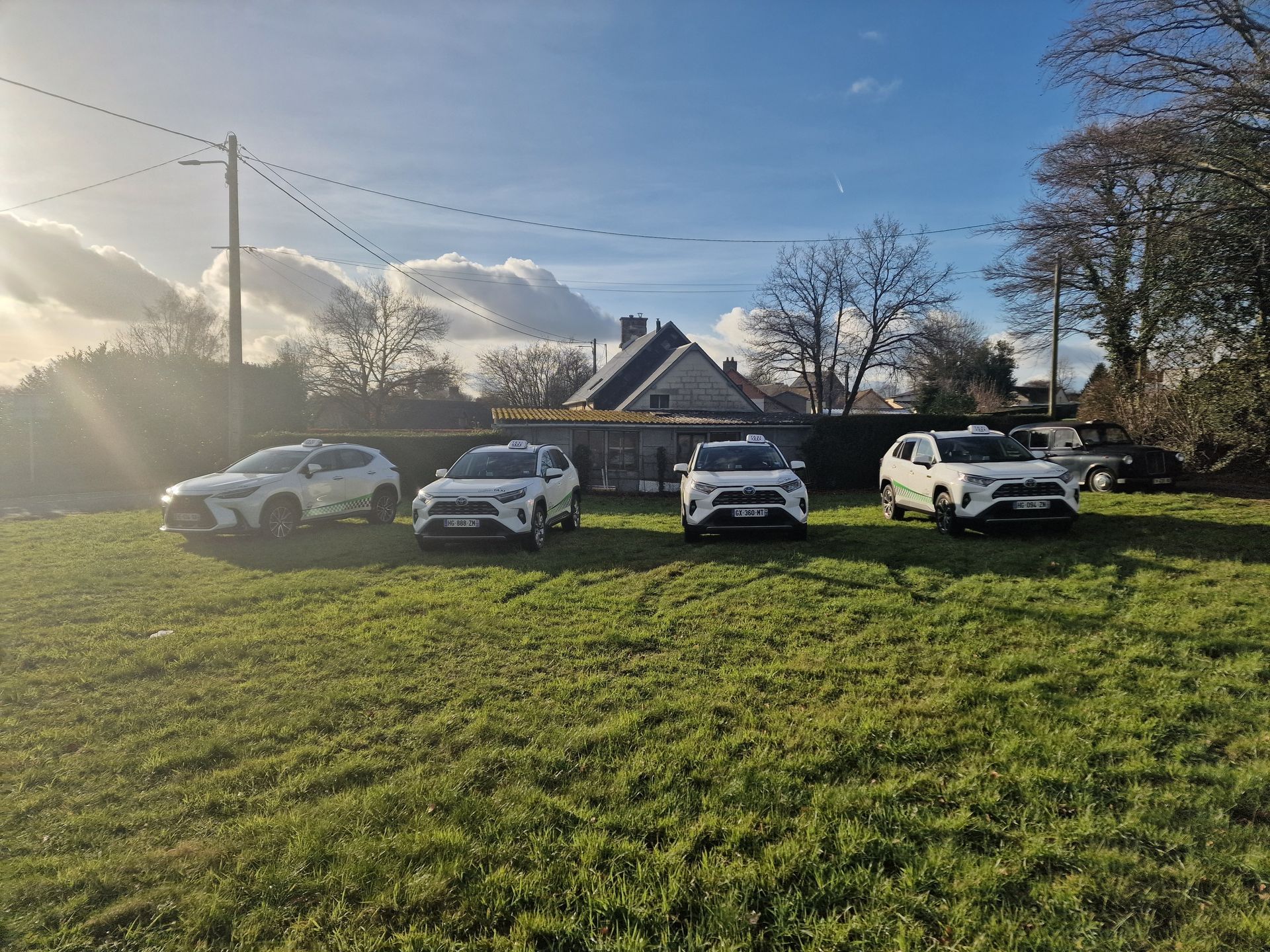 Quatre SUV garés en file indienne sur un terrain herbeux devant une maison.