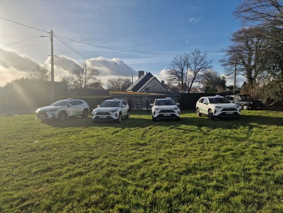 Quatre SUV garés en file indienne sur un terrain herbeux devant une maison.