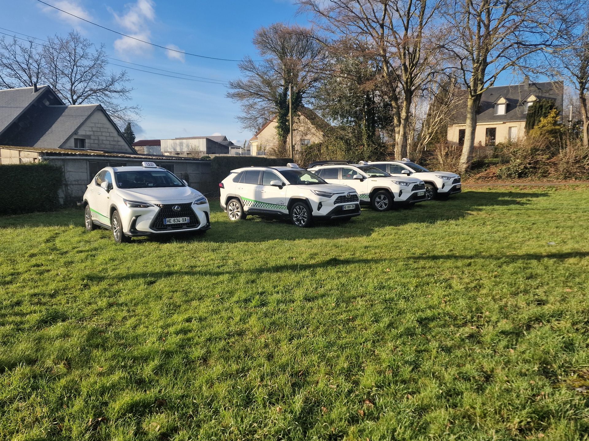 Quatre SUV garés en rang sur un terrain herbeux devant une maison d'habitation rurale.