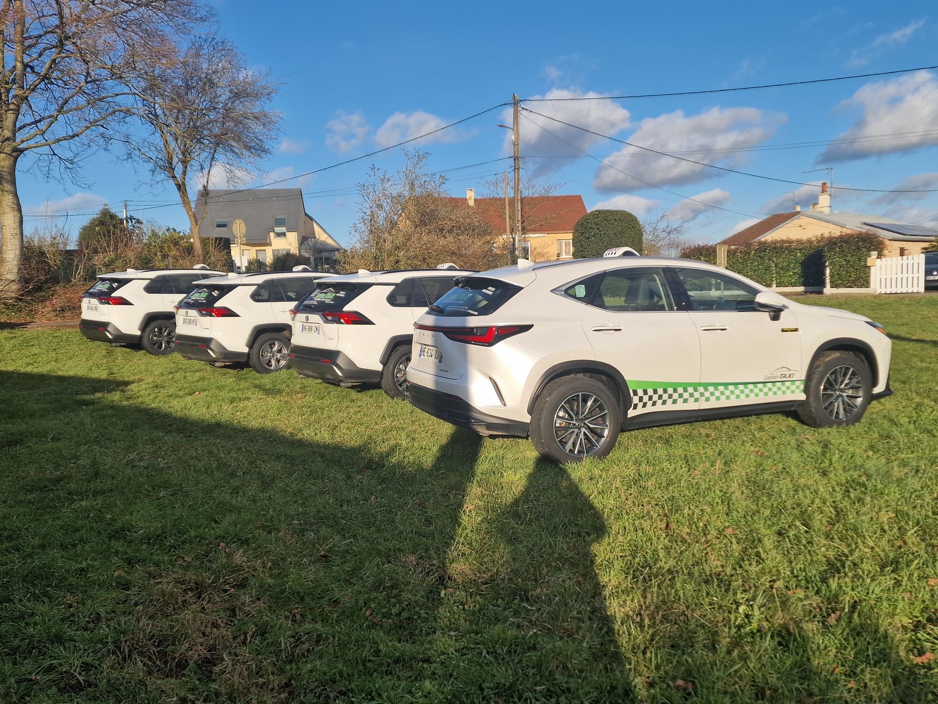 Quatre SUV Lexus étaient garés en rangée sur un terrain herbeux devant des maisons d'habitation.