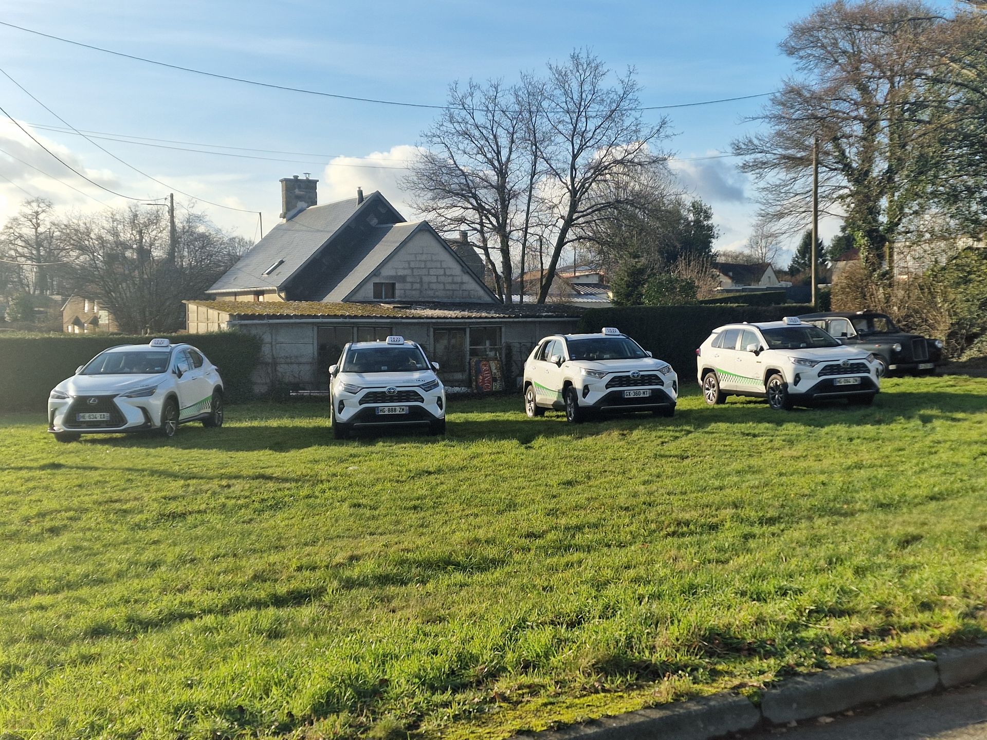 Quatre SUV, Toyota et Lexus, étaient garés en rang sur un terrain herbeux devant une maison.