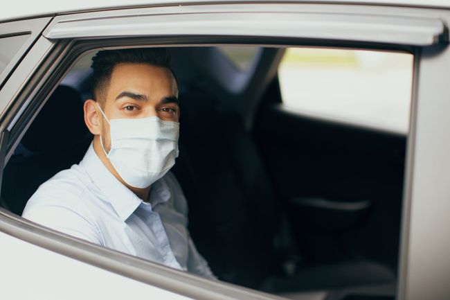 Un homme portant un masque facial dans une voiture, regardant la caméra.