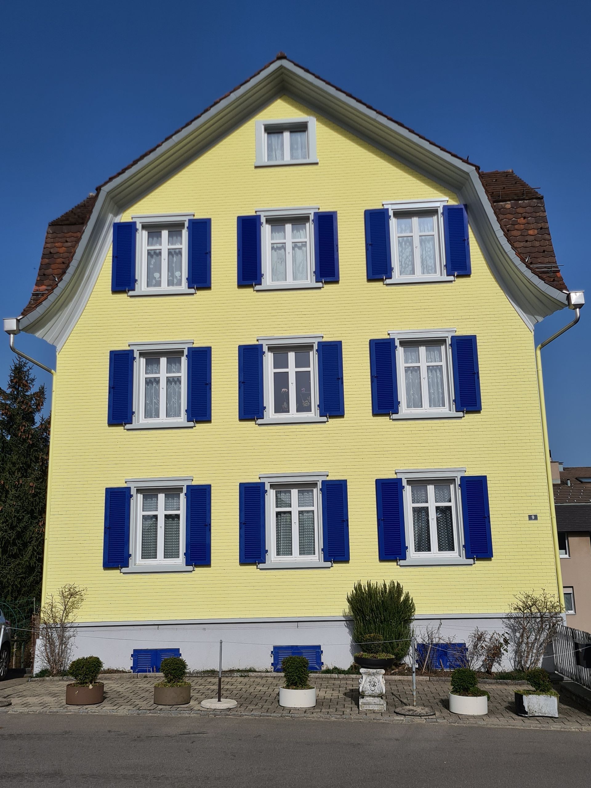 Gelbes mehrstöckiges Gebäude mit blauen Fensterläden und rotem Dach.