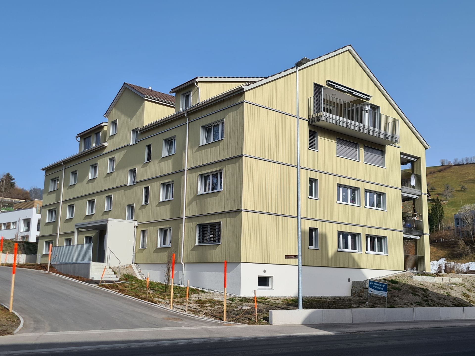 Gelbes, mehrstöckiges Wohngebäude mit Balkonen, am Hang gelegen.