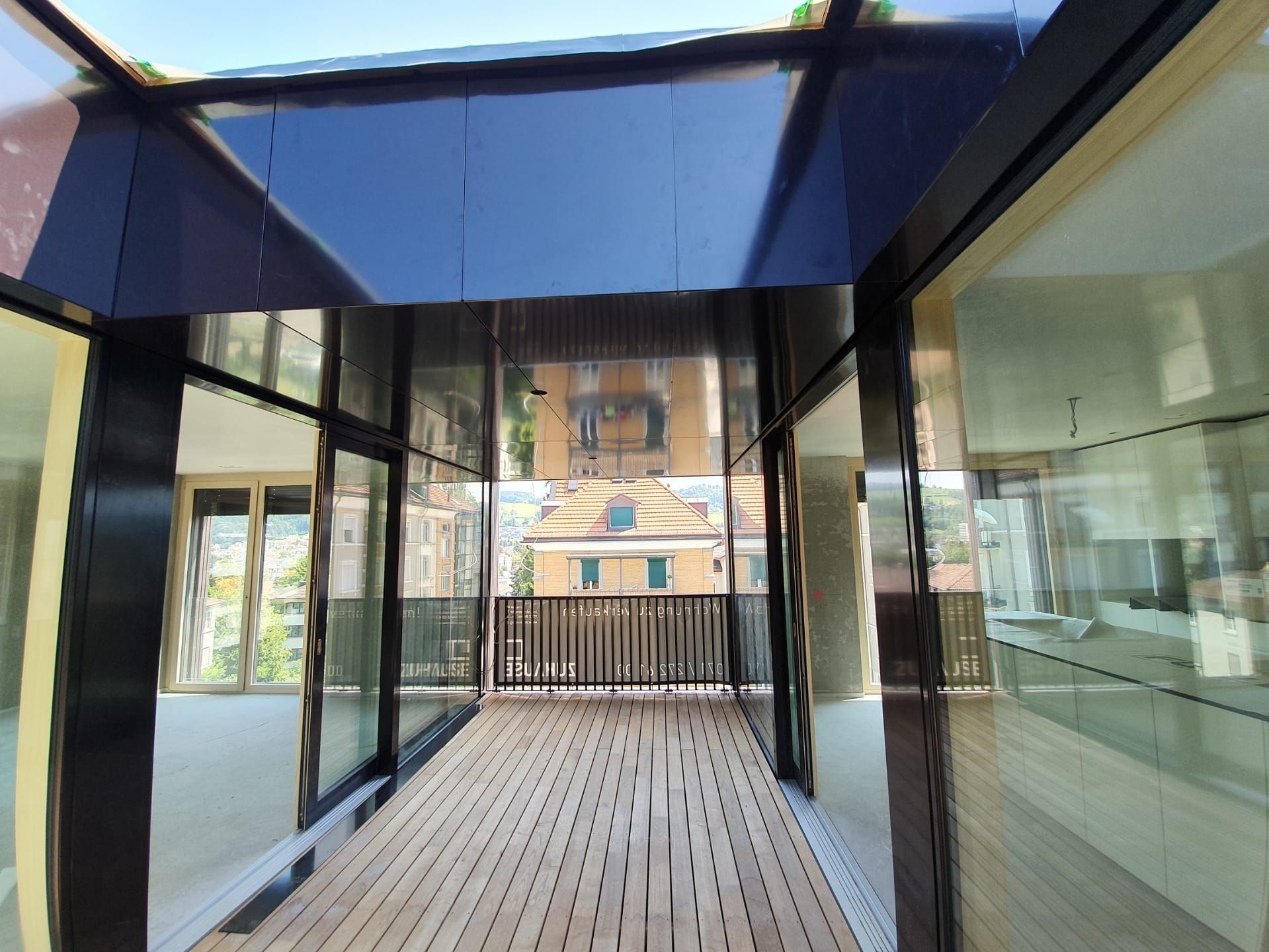 Verglaste Dachkonstruktion mit Holzsteg, Blick auf die Stadt mit ihren Gebäuden und Balkon.