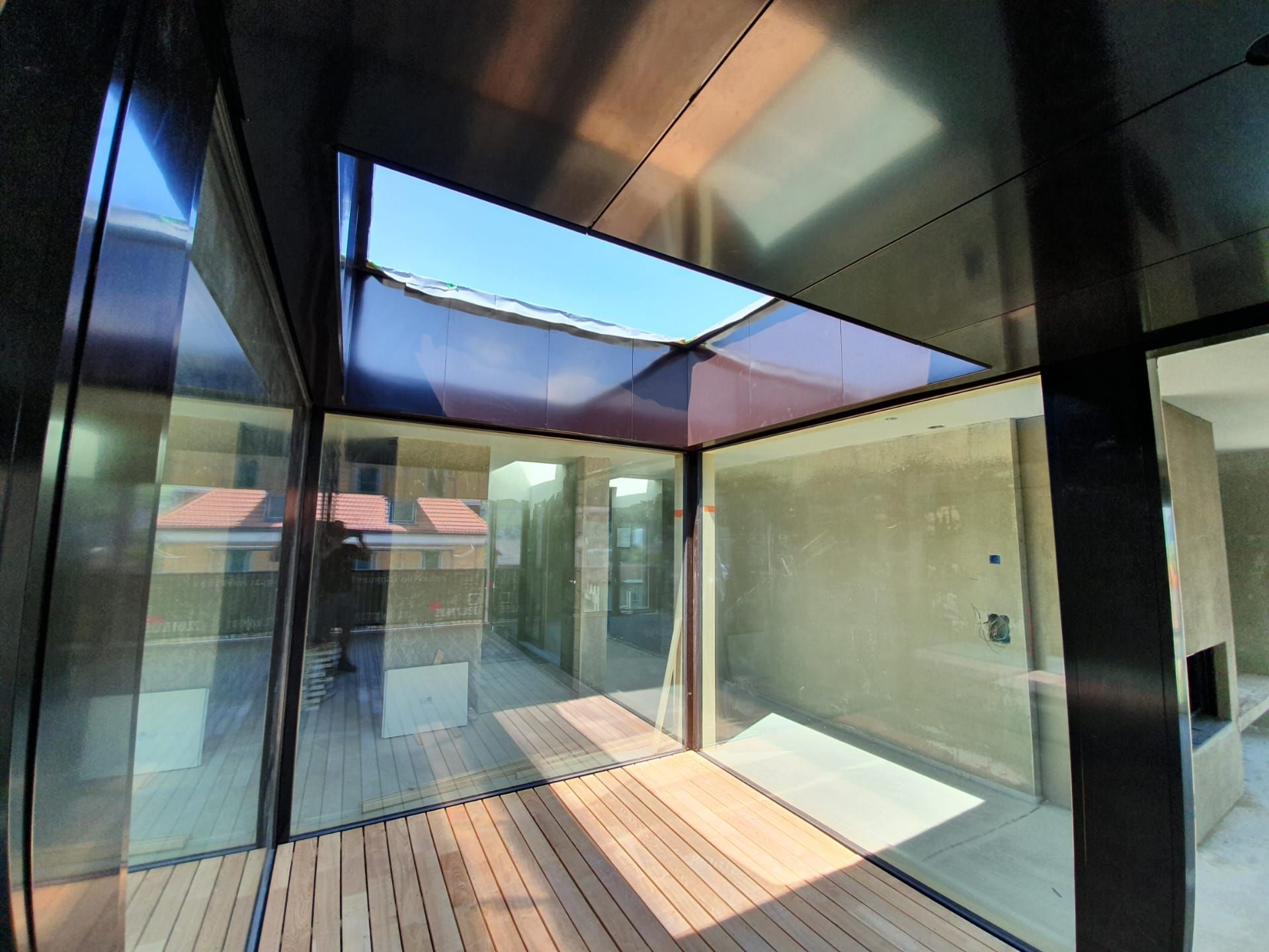 Modernes Zimmer mit Holzboden, Glaswänden und Oberlicht mit Blick auf den blauen Himmel.