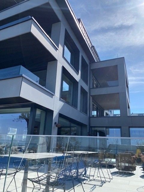 Holzchalets an einem Hang mit Kirchturm, üppigem Grün und bewölktem Himmel.