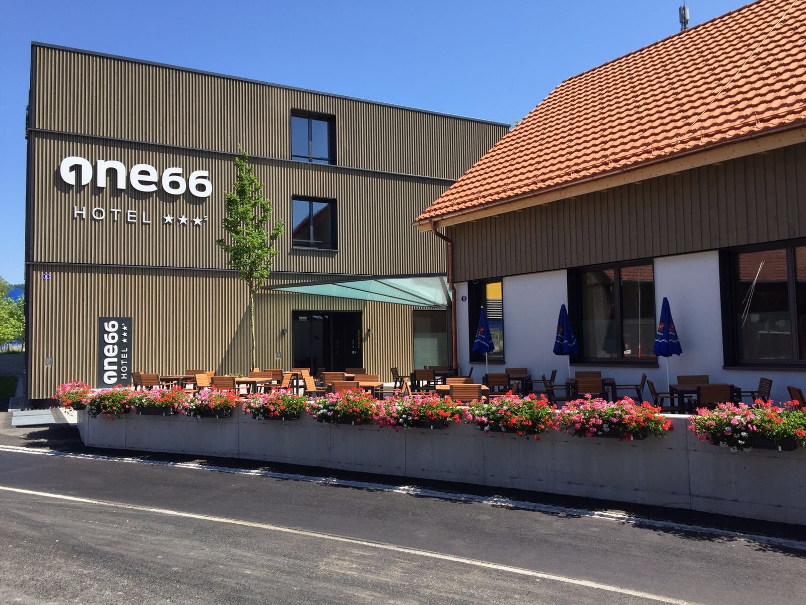 Das Hotel One66 mit Holzfassade, Blumenkästen und einem angrenzenden Restaurant bietet einen sonnigen Außenbereich.