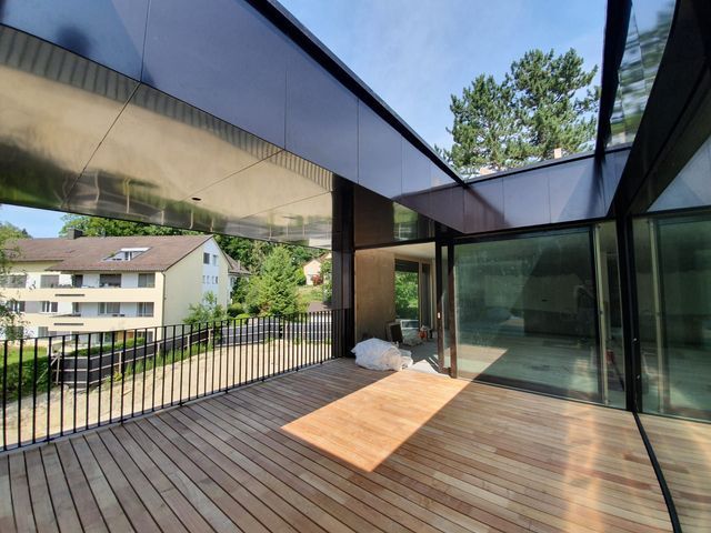 Moderner Balkon mit Holzboden, Glaswänden und Metalldach mit Blick auf ein Wohngebiet.