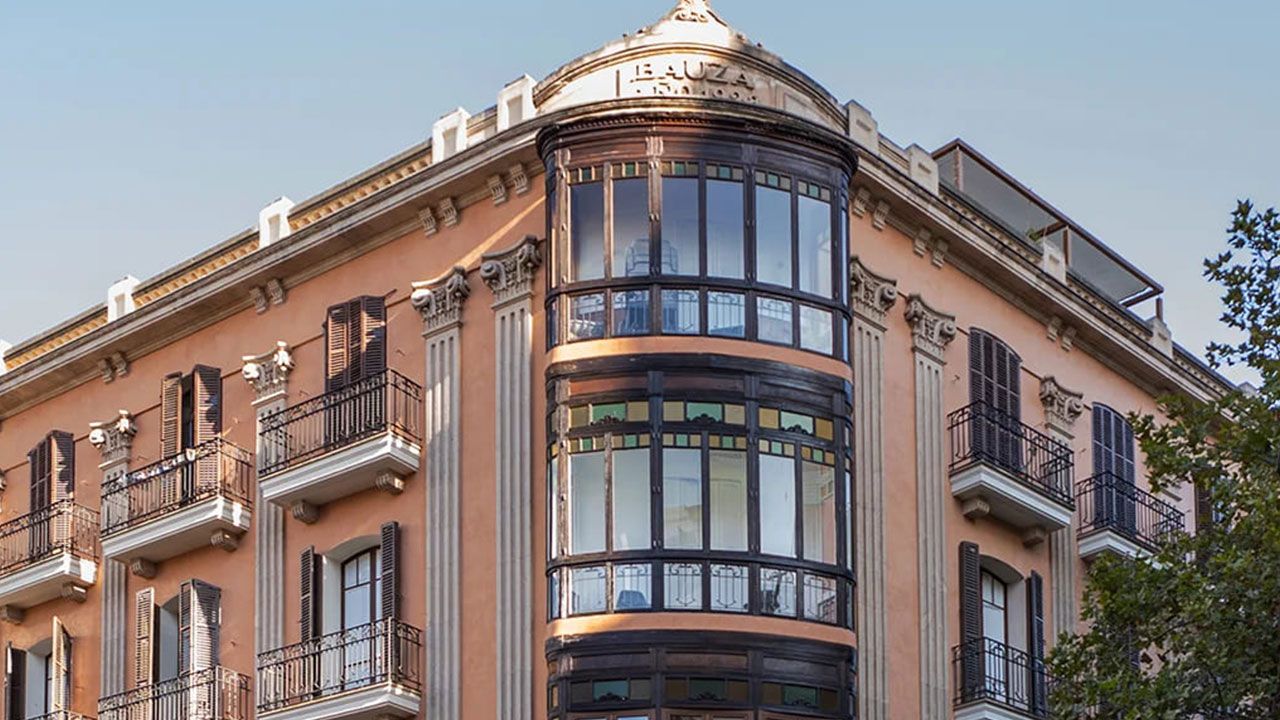 Edificio esquinero ornamentado con un ventanal curvo de cristal y balcones de hierro forjado