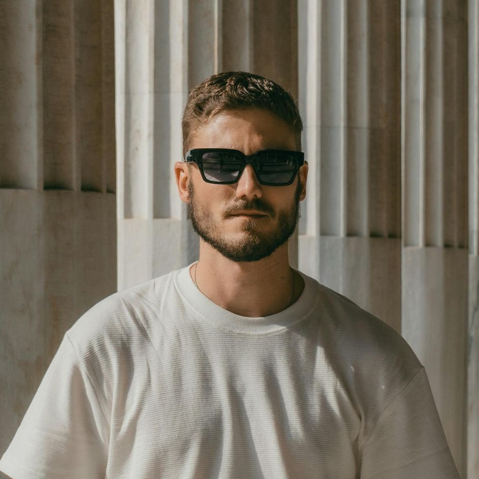 A man with a beard wearing sunglasses and a white shirt.