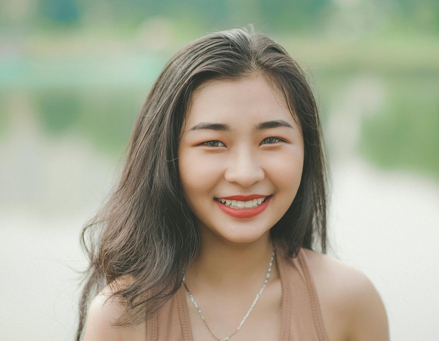 A woman with long hair is smiling and wearing a necklace.