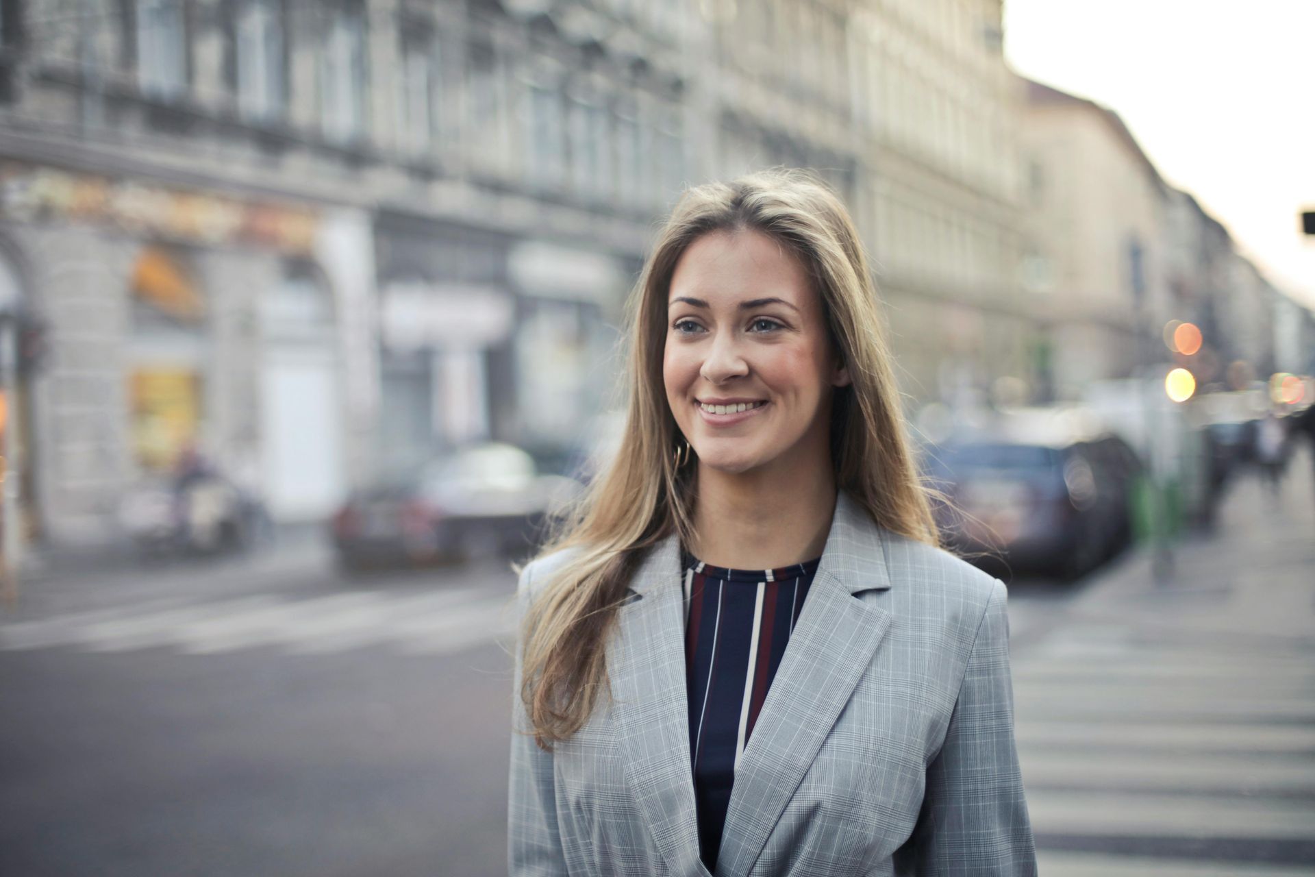 A woman in a suit is standing on a city street and smiling.