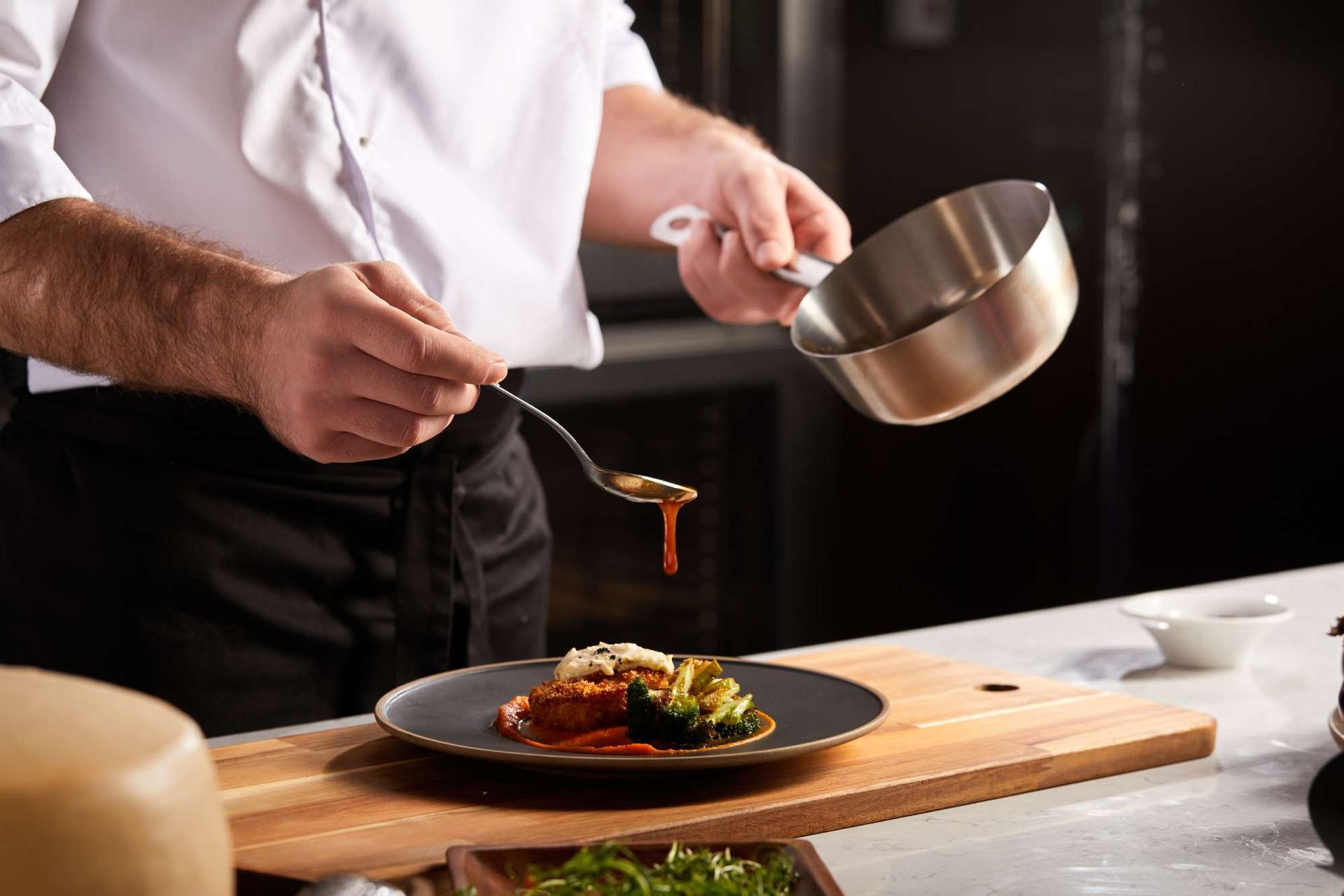 A chef is adding sauce to a plate of food with a spoon.